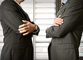 Two men in suits facing eachother with their arms crossed