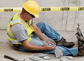 Construction worker sitting on the ground grabbing his knee in pain