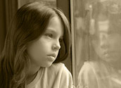 Young girl looking out a window with a sad expression